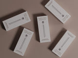 Brow Roller aus Edelstahl auf einem Marmortablett neben einem Augenbrauenserum