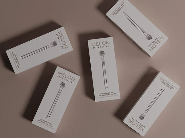 Brow Roller aus Edelstahl auf einem Marmortablett neben einem Augenbrauenserum